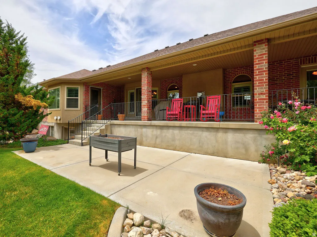 Expansive concrete patio with integrated stairs leading to a covered porch with brick columns and wrought iron railing