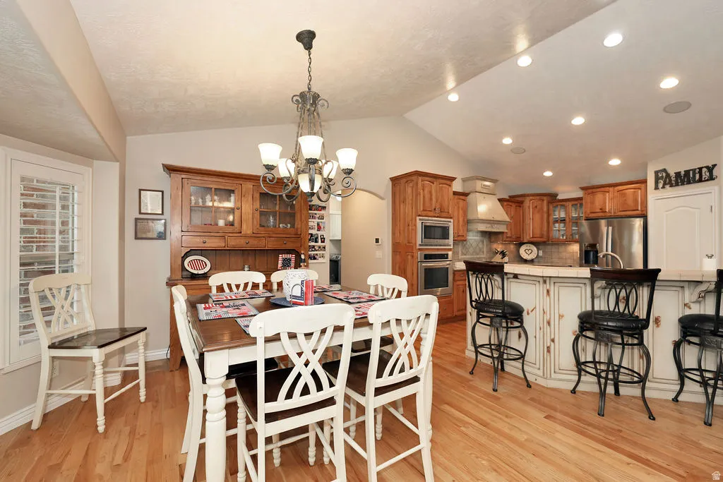 Hardwood flooring throughout a dining area with a multi-light chandelier, offering a partial view of the kitchen