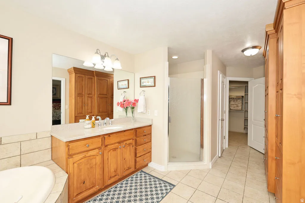 Bathroom featuring a wood-finish vanity with an integrated sink and light-toned countertop, a glass-enclosed shower, a built-in bathtub with tiled surround, tile flooring, and integrated wood-finish cabinetry