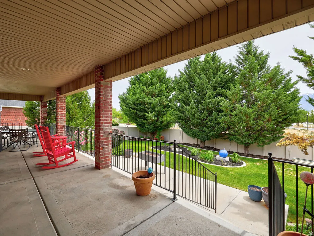 Covered concrete patio featuring brick columns and a black metal railing