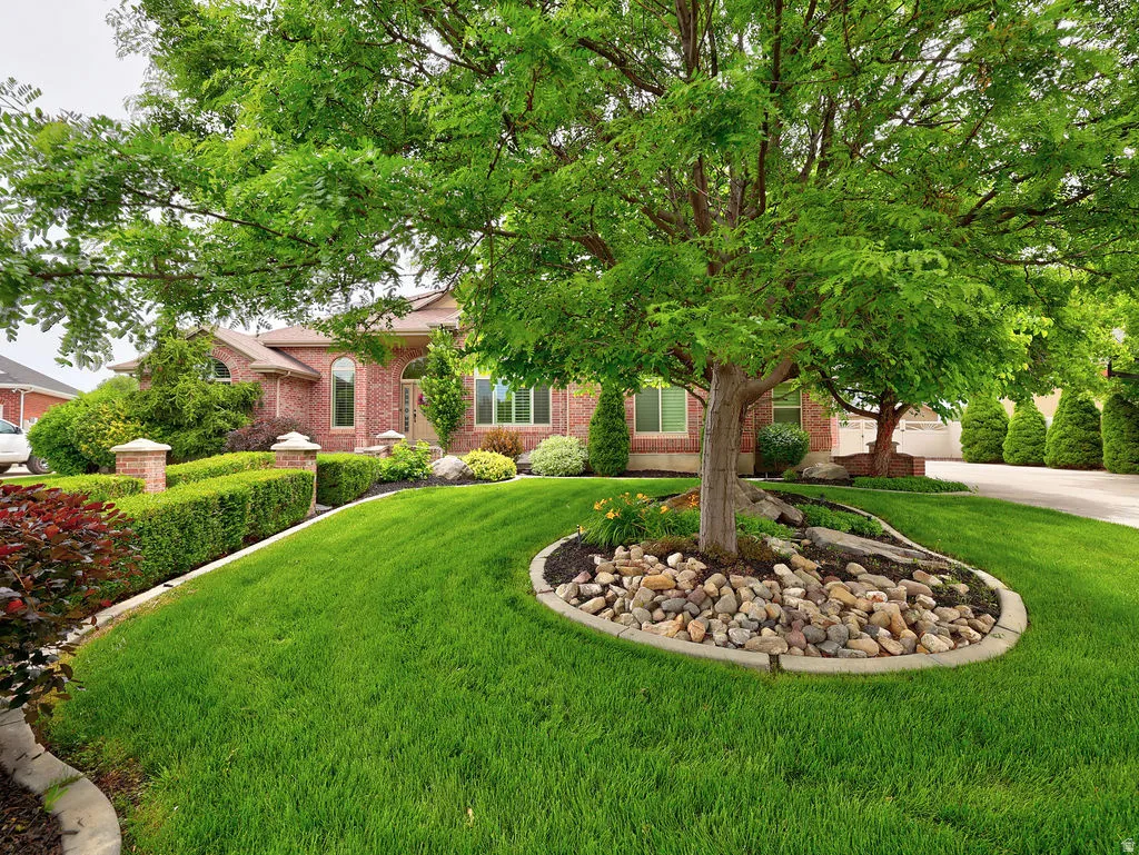 Brick exterior featuring an arched entryway, multiple windows, and a manicured lawn with mature trees and shrubbery
