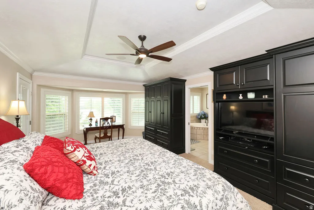 Bedroom featuring a tray ceiling with crown molding, a ceiling fan, and a bay window with plantation shutters