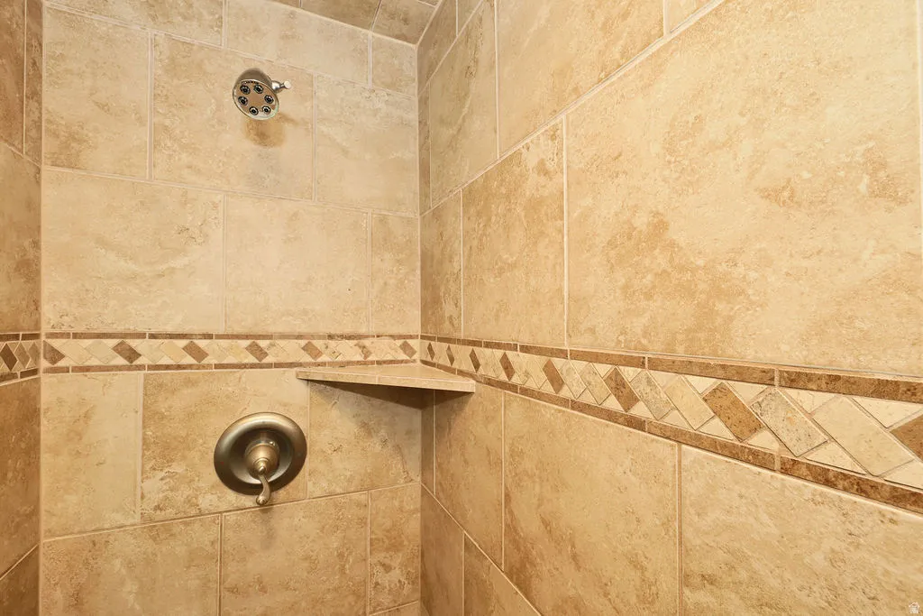 Tile shower featuring a decorative accent band, integrated corner shelf, shower head, and bronze-finish plumbing fixtures