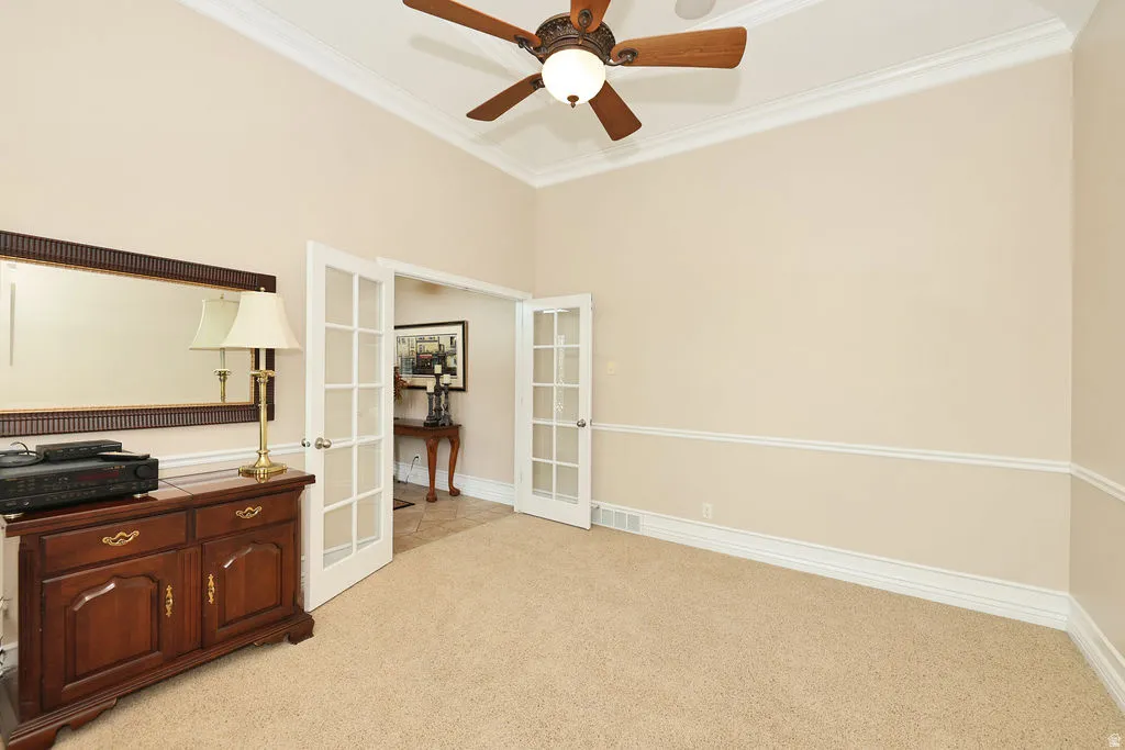 Carpeted room featuring a ceiling fan with integrated lighting, crown molding, chair rail molding, and french doors with glass panels