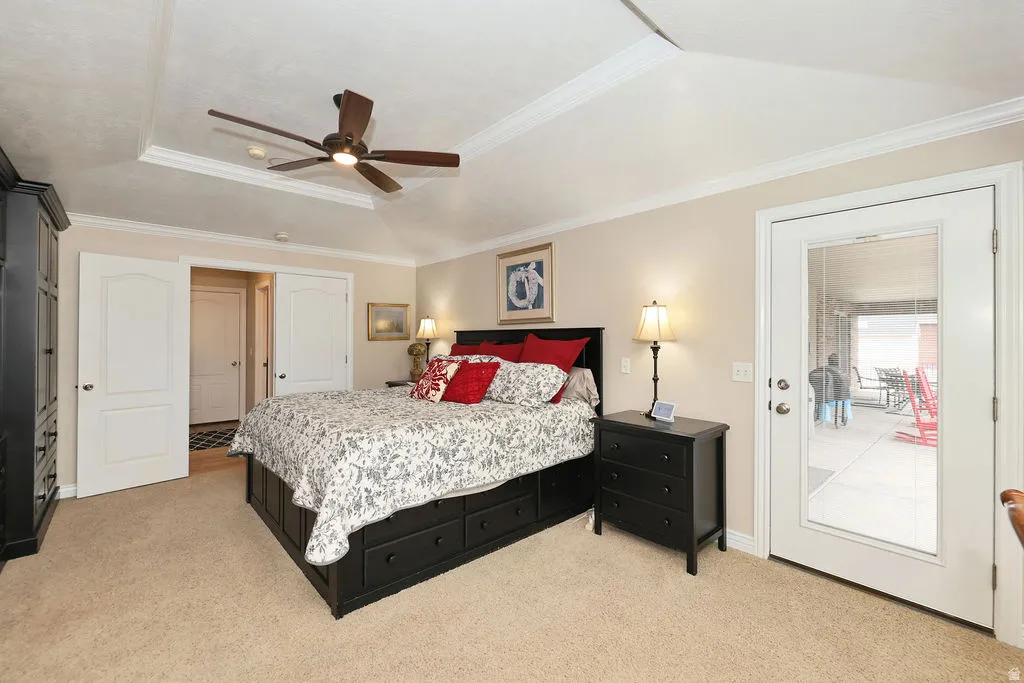 Bedroom featuring a tray ceiling with crown molding, a ceiling fan, and light beige carpeting
