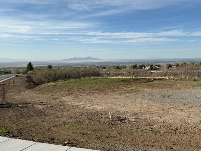 Expansive land parcel featuring partial ground cover, a newly installed sidewalk, and a distant mountain range backdrop