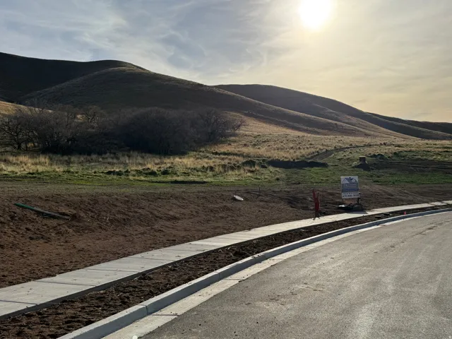 Paved road with new concrete curb and sidewalk, alongside a natural hillside landscape
