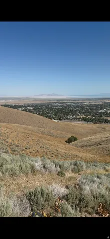 Expansive parcel featuring a sloped terrain with natural vegetation, offering distant city and mountain scenery under a clear sky