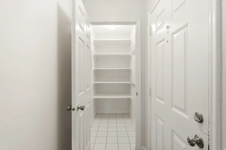 Front door with adjacent pantry. Recessed lighting illuminating the pantry, multiple built-in shelving units, and a tiled floor