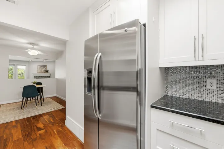 Stainless steel refrigerator, white cabinetry, dark stone countertop, mosaic tile backsplash, and wood-finish flooring
