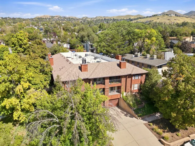 Brick exterior with multiple balconies, a sloped driveway, and mature landscaping