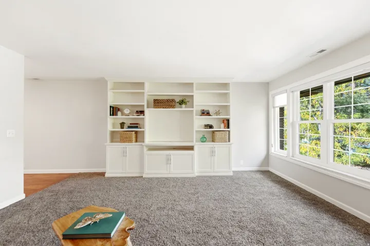 Built-in white shelving and cabinetry, large windows, light gray wall paint, and gray carpet