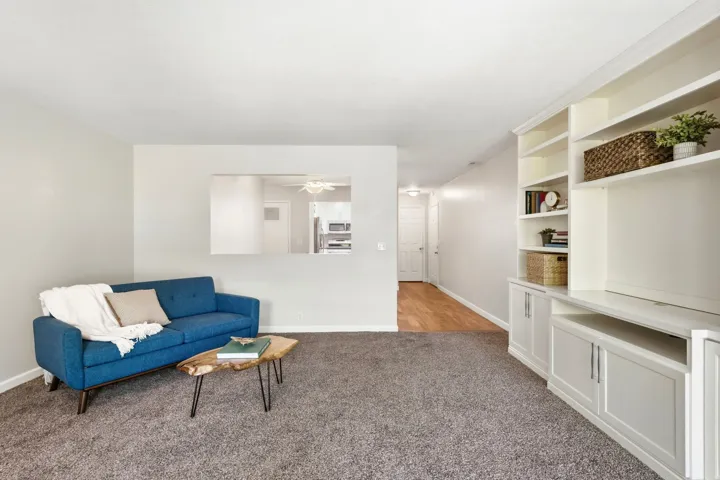 Living area featuring built-in shelving, white cabinetry, a pass-through window, and wood-finish flooring