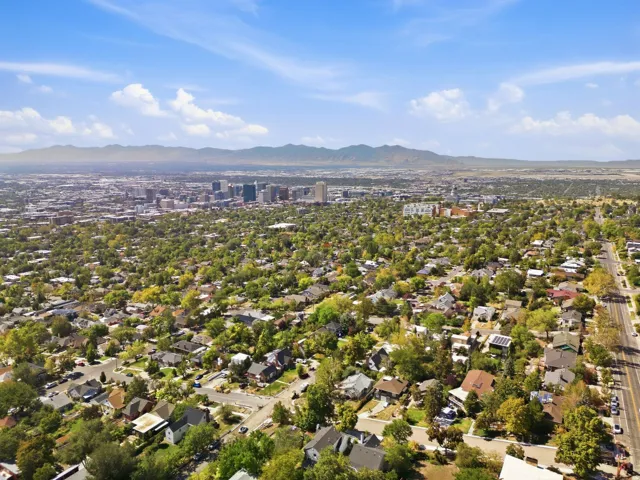 Expansive urban landscape with a mountain backdrop, showcasing a residential area with mature trees and a distant city skyline