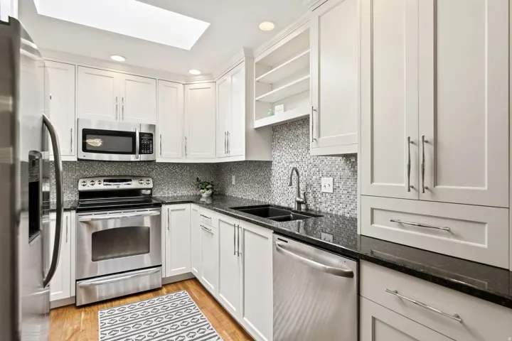 White cabinetry with stainless steel appliances, black countertops, and a mosaic tile backsplash