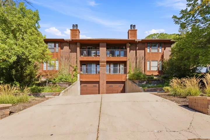 Brick exterior with multiple balconies, two attached garages, and a sloped concrete driveway