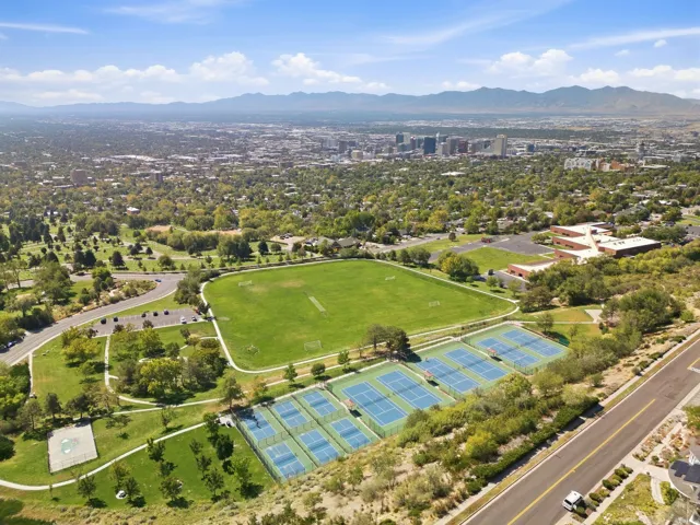 Expansive park grounds with multiple tennis courts, a large sports field, and a distant cityscape backdrop