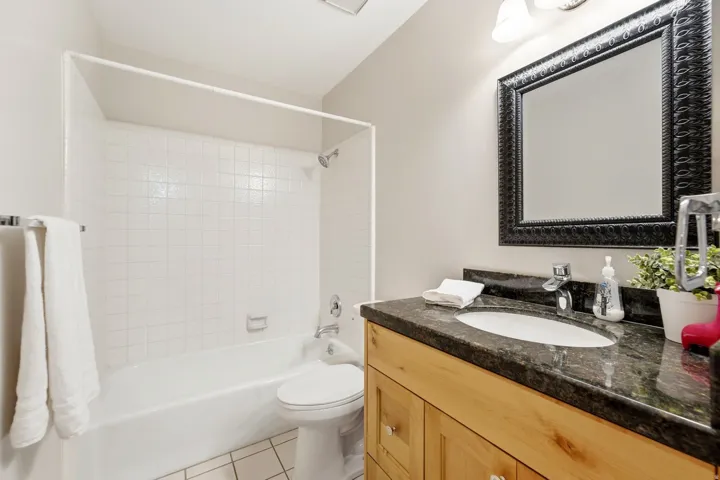 Bathroom featuring a wood-finish vanity with a dark countertop and integrated sink, a large framed mirror, and a tiled shower-tub combination