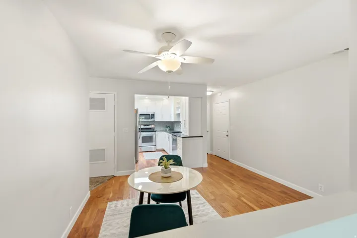 Wood-finish flooring throughout, white walls, and a recessed kitchen area