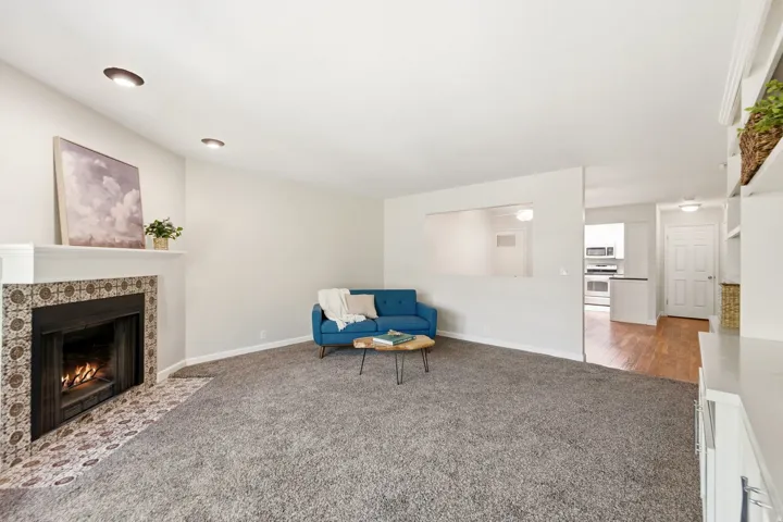 Carpeted living area with a fireplace featuring a decorative tile surround and hearth, built-in shelving, recessed lighting, and a pass-through opening to an additional room