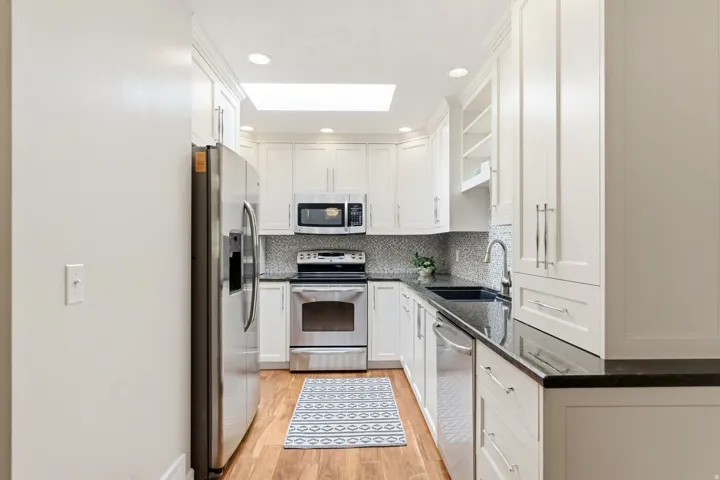 White cabinetry, stainless steel appliances, dark countertops, a mosaic tile backsplash, and wood-finish flooring