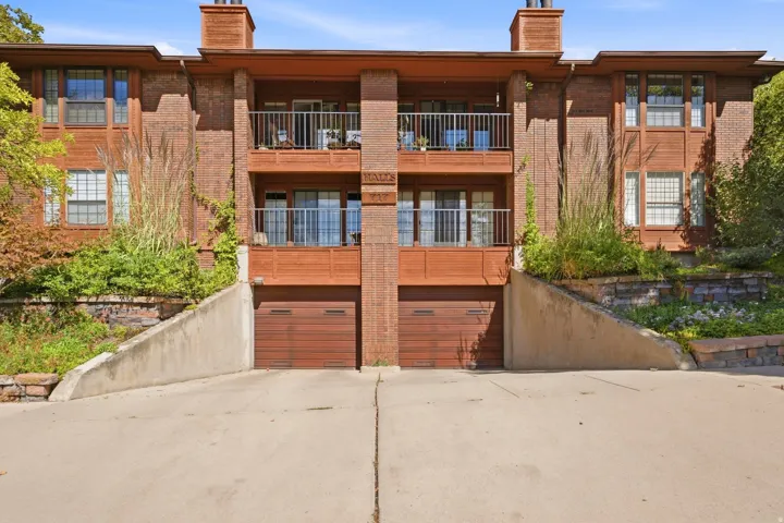 Brick exterior featuring multiple balconies with metal railings, two integrated garages with wood-finish doors, and a concrete driveway
