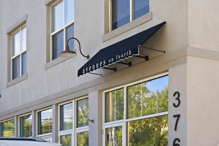 Stucco exterior with multiple windows, a prominent black awning, and large ground-level display windows