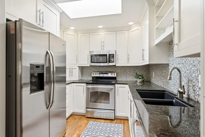 White cabinetry, wood-finish flooring, stainless steel appliances, dark stone countertops, and a mosaic tile backsplash