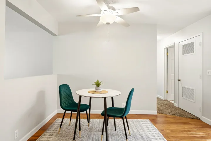 Hardwood-style flooring with a decorative area rug, overhead ceiling fan with lighting, and white baseboards