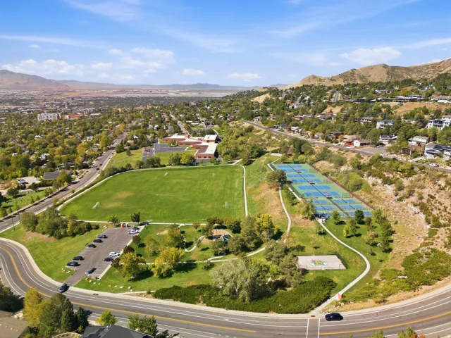 Expansive green athletic field, multiple tennis courts, paved walking paths, and a substantial parking area