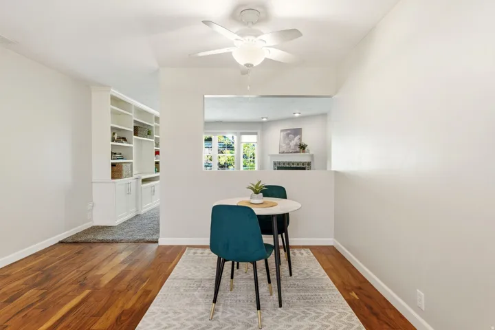 Wood-finish flooring, built-in shelving, white walls, and a ceiling fan with integrated lighting