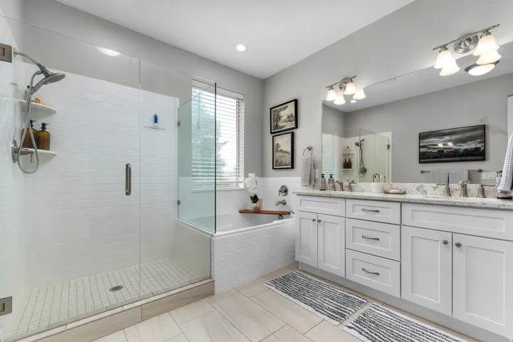 Spacious bathroom featuring a glass-enclosed shower with white subway tile, a separate built-in bathtub, and a double vanity with stone countertops and white cabinetry