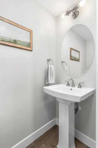 White ceramic pedestal sink with brushed nickel faucet, an oval mirror, and overhead vanity lighting