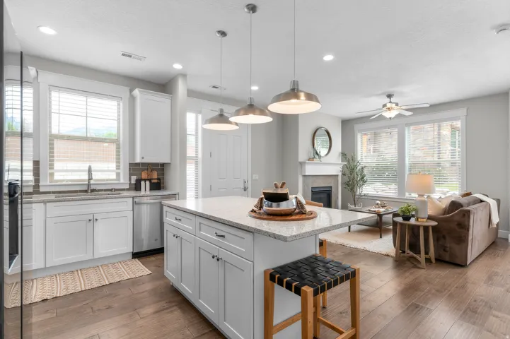 Open-concept living space featuring wood-finish flooring, a kitchen island with stone countertop, stainless steel appliances, white cabinetry, and a fireplace with a mantel