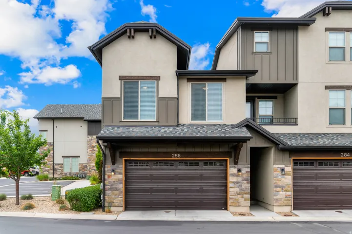 Modern townhome exterior featuring a neutral stucco and stone facade, dark trim, an integrated garage, and contemporary windows