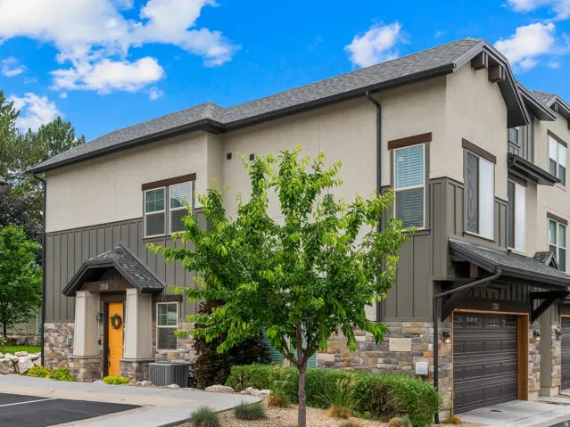 Multi-level townhome featuring a stucco and stone facade, dark wood-finish garage doors, and a covered entry with a vibrant front door