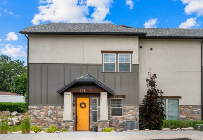 Contemporary multi-level residence featuring a prominent orange entry door, stone veneer detailing, vertical panel siding, and stucco finishes