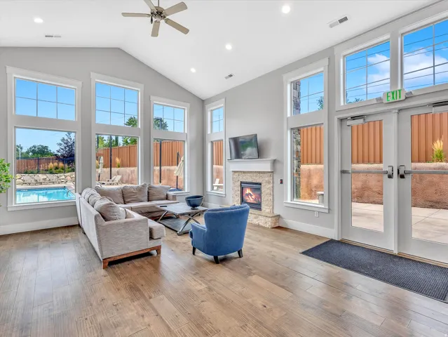 Spacious living area featuring a vaulted ceiling with a ceiling fan, abundant natural light through multiple large windows, and durable wood-finish flooring