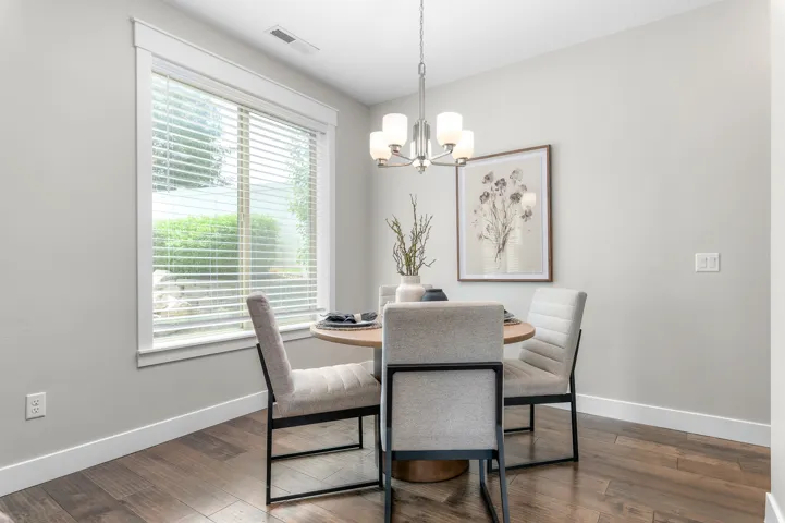 Dining area featuring wood-finish flooring, a large window with blinds, a modern chandelier, and light gray wall paint