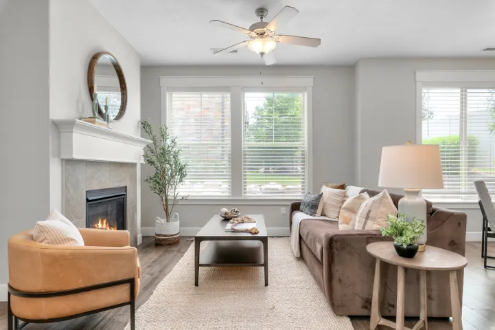 Spacious living area featuring wood-finish flooring, a white mantel fireplace with tile surround, and a ceiling fan with integrated lighting