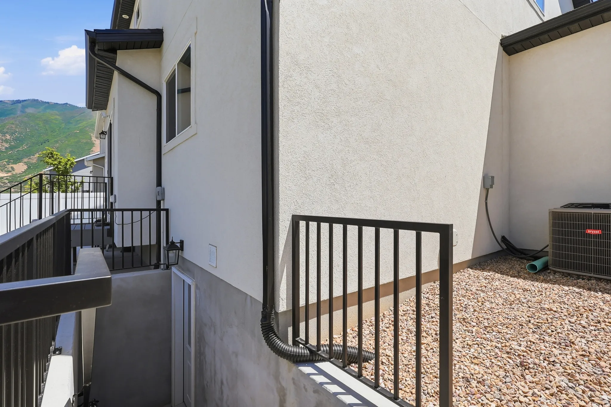 Exterior stucco siding with a lower-level entrance, featuring black metal railings and an exterior light fixture
