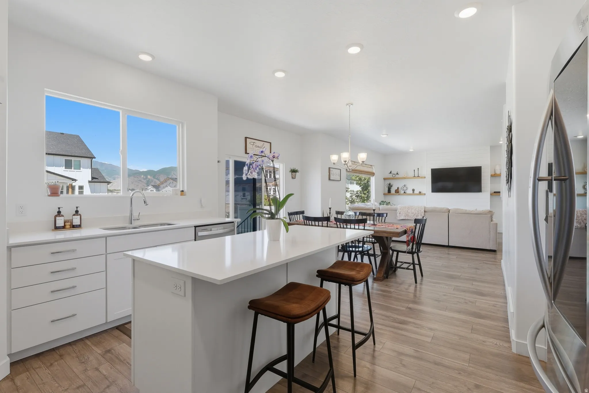 Open-concept living space featuring a kitchen island with seating, wood-finish flooring, recessed lighting, and a window framing distant mountains