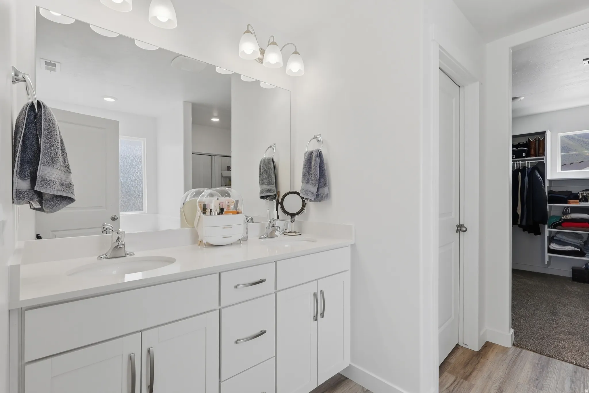 Dual vanity featuring white cabinetry, integrated sinks, chrome fixtures, and a large wall-mounted mirror