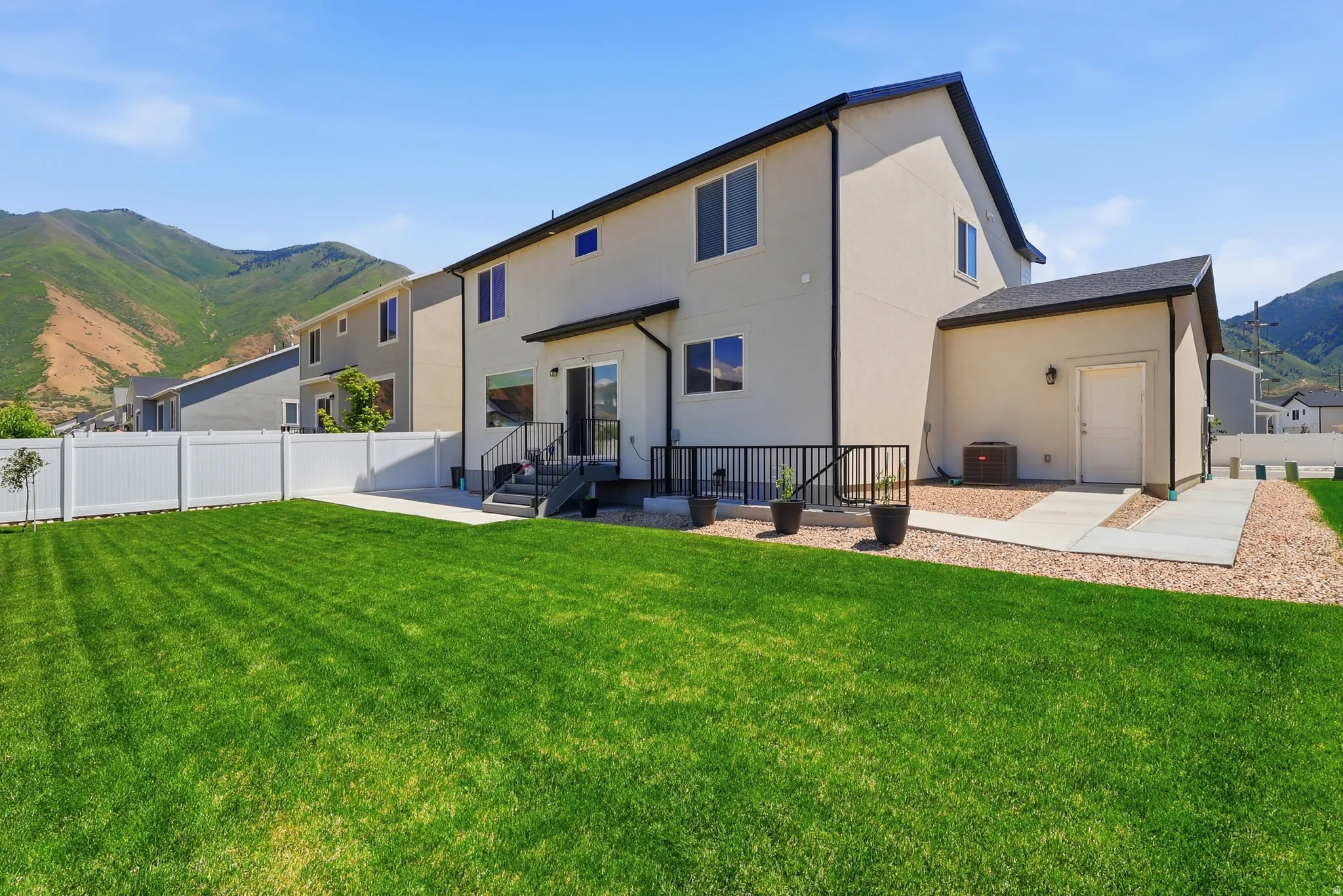 Rear exterior featuring a spacious lawn, white vinyl fencing, a concrete patio, and a gravel perimeter