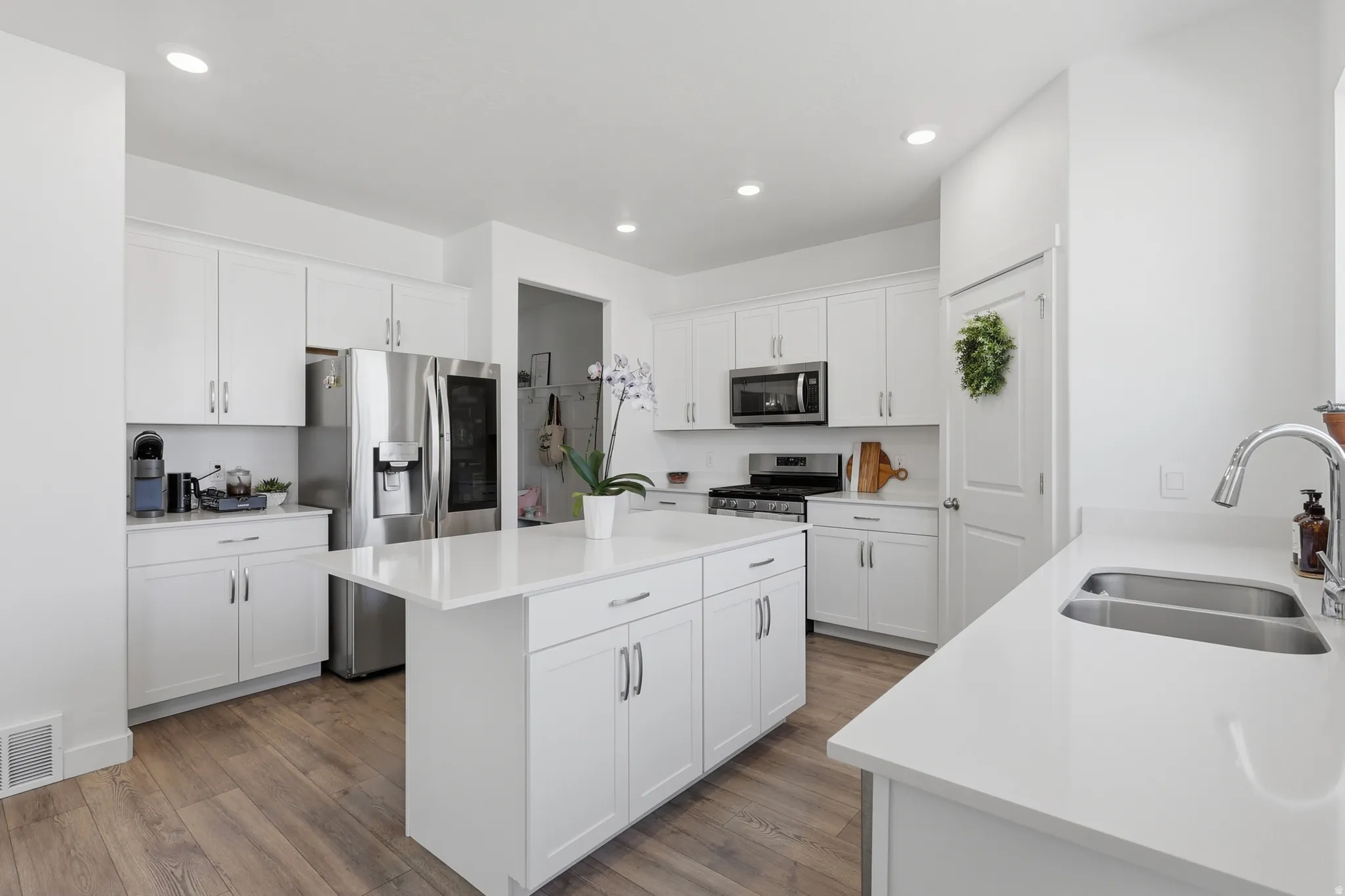 Bright kitchen featuring white cabinetry, a large kitchen island, stainless steel appliances, wood-finish flooring, and recessed lighting