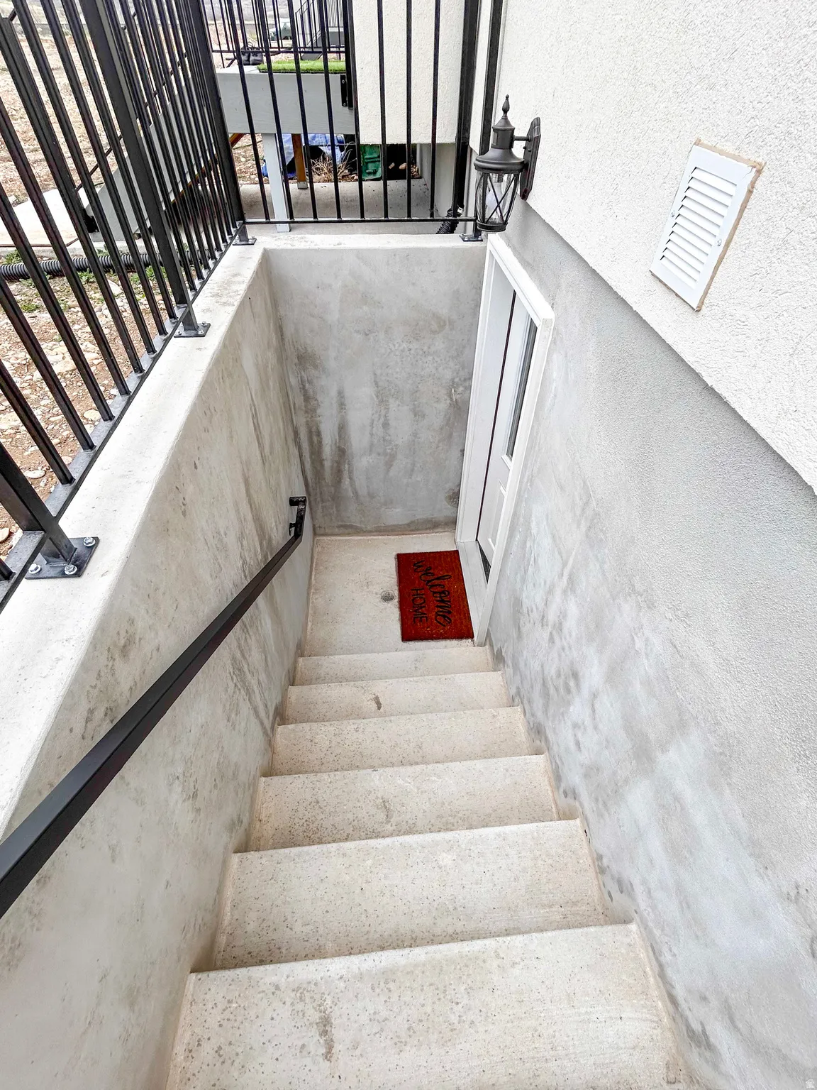 Exterior concrete stairs with a black metal handrail leading to a white door