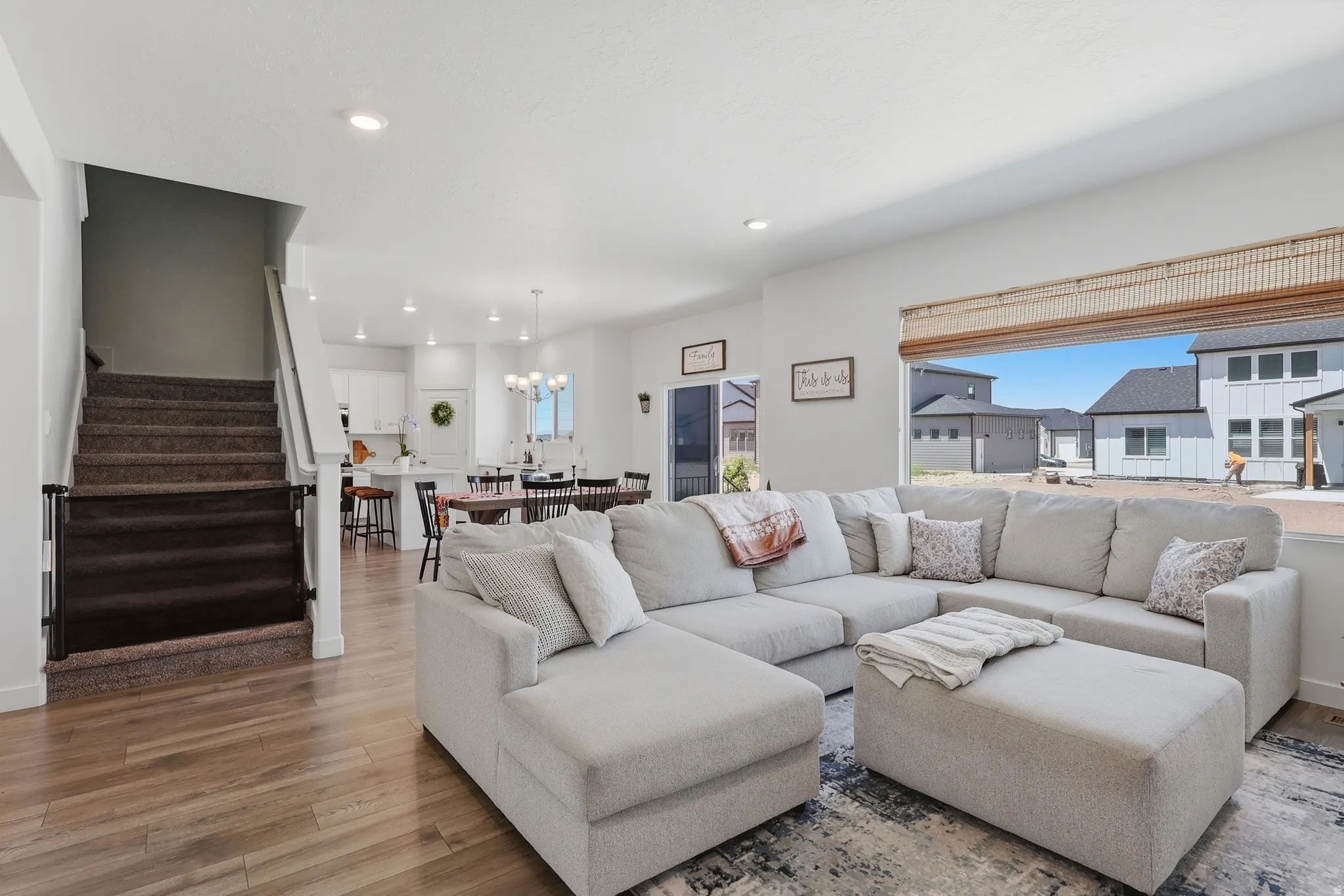 Open-concept living area with wood-finish flooring, recessed lighting, and a staircase with carpeted treads