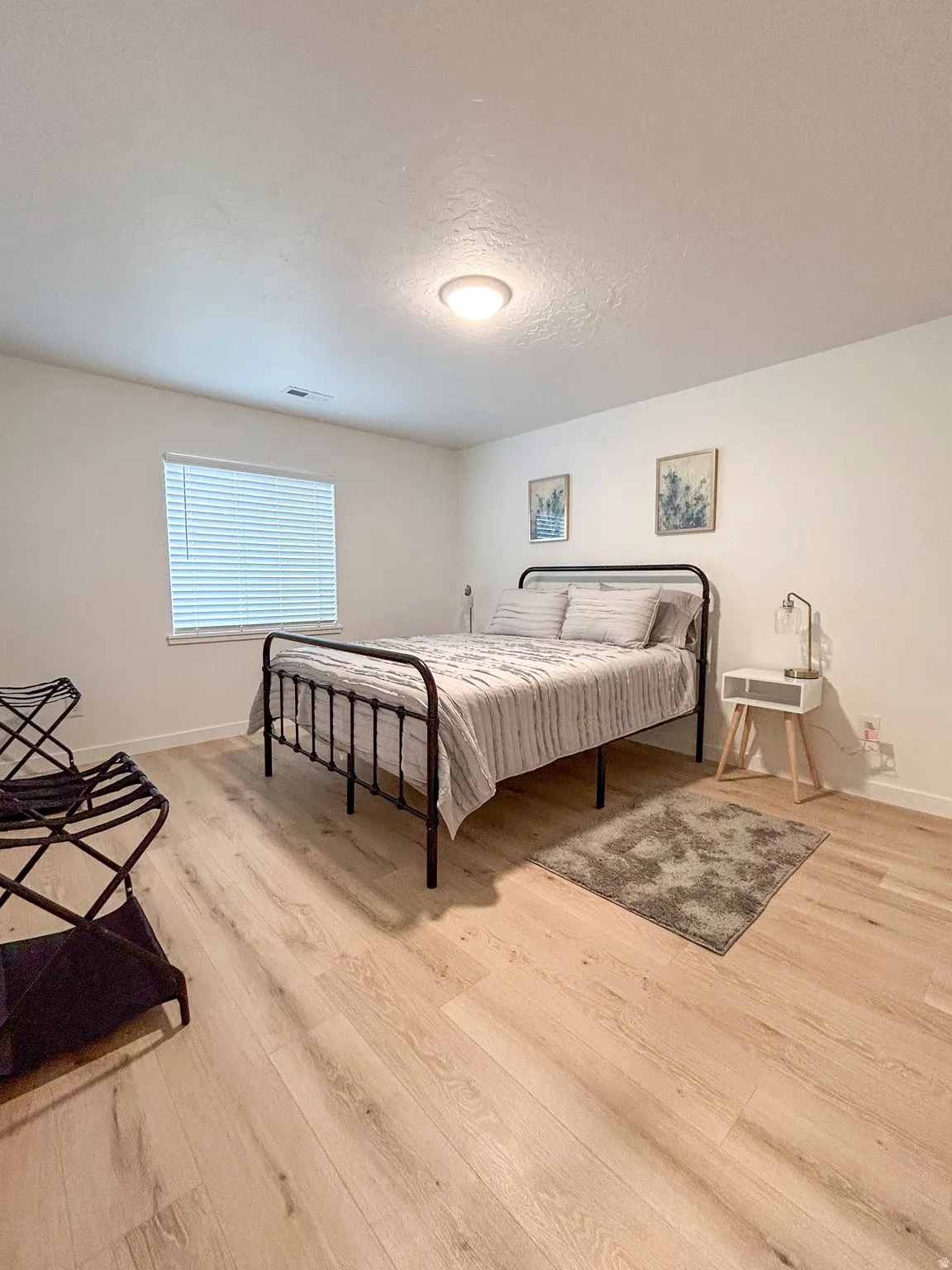 Room with light wood-finish flooring, white walls, and a window featuring blinds