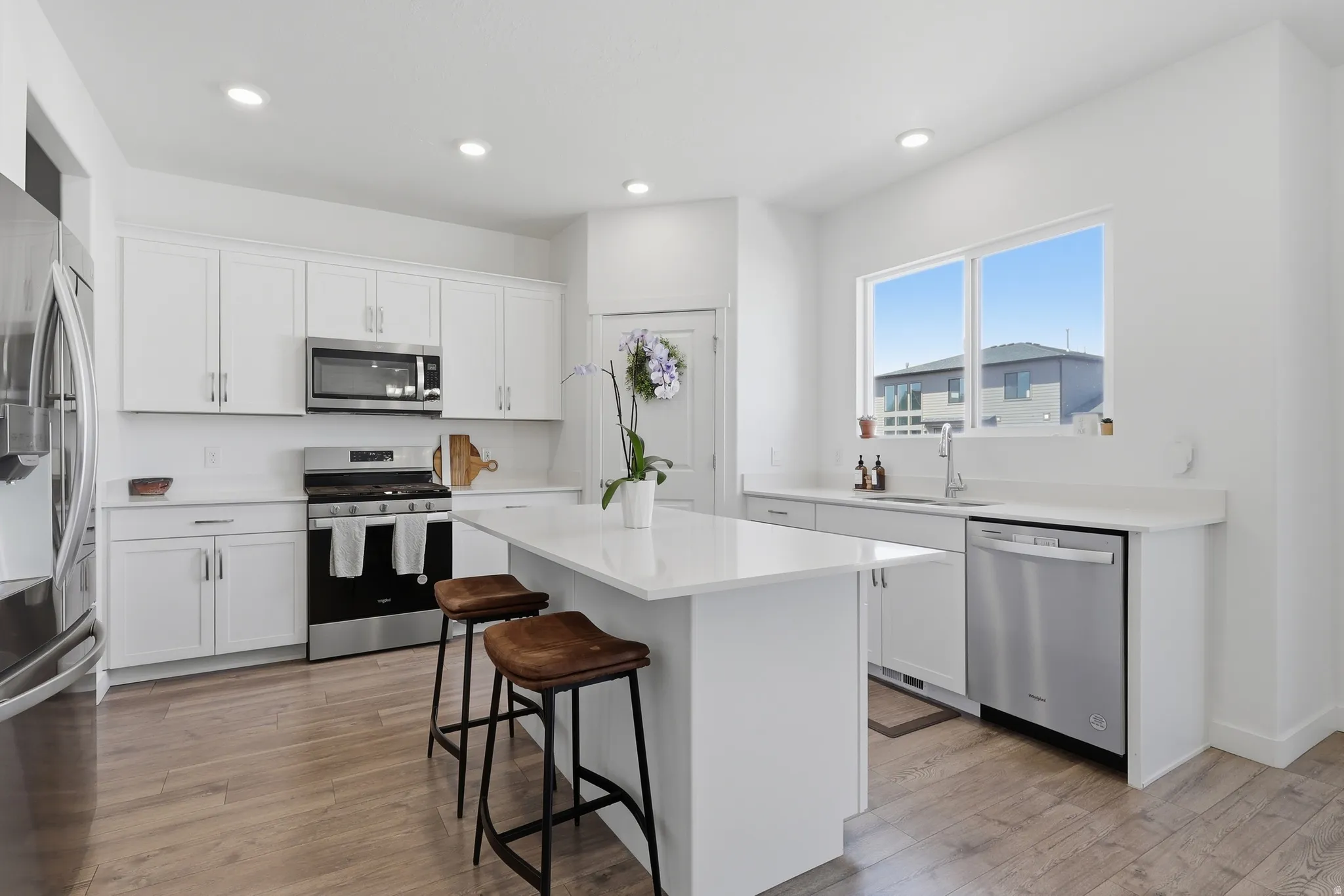 Modern kitchen featuring white cabinetry, a central island, stainless steel appliances, wood-finish flooring, and a large window