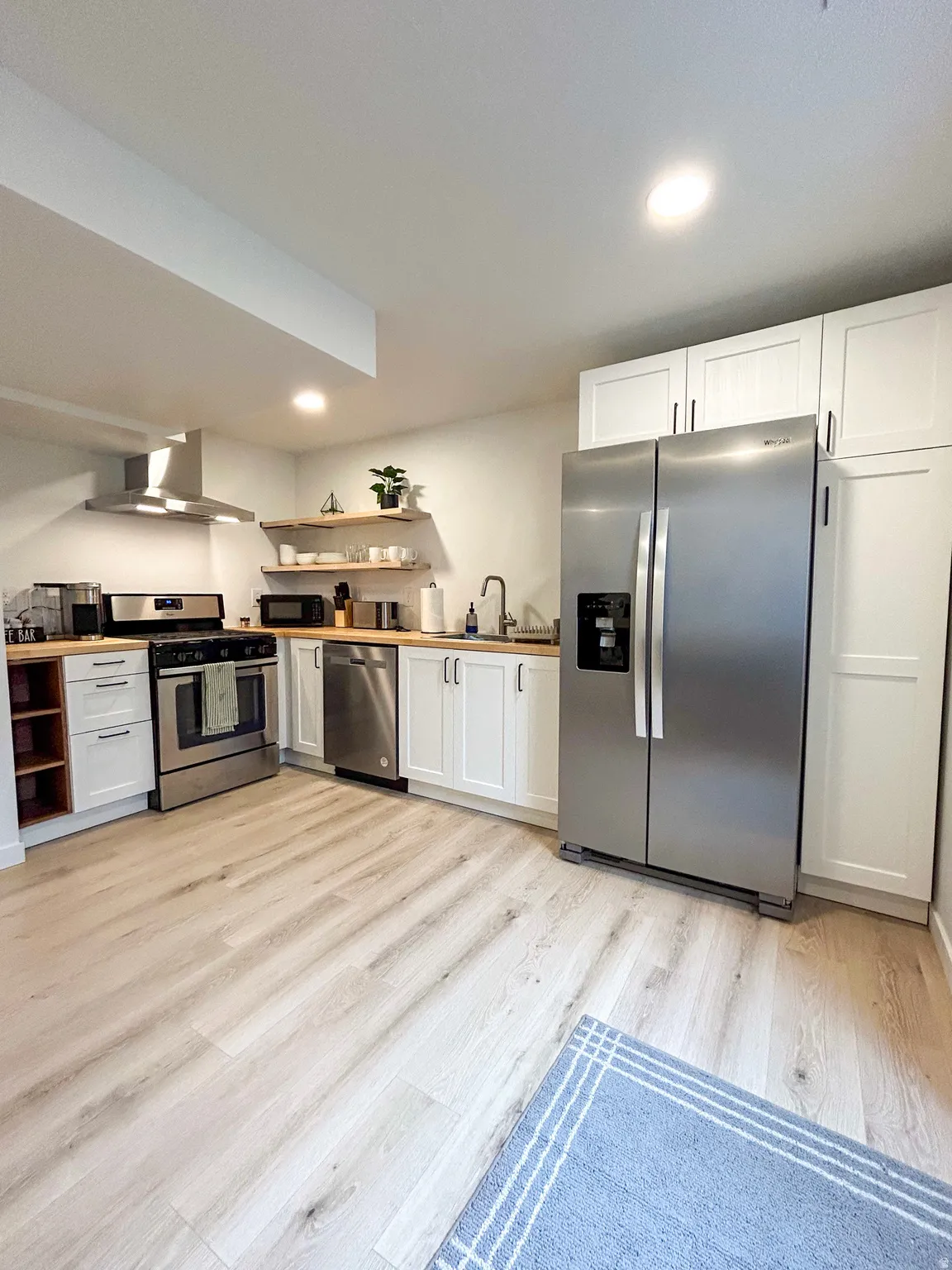 Modern kitchen featuring stainless steel appliances, white cabinetry, wood-finish countertops, and wood-finish flooring